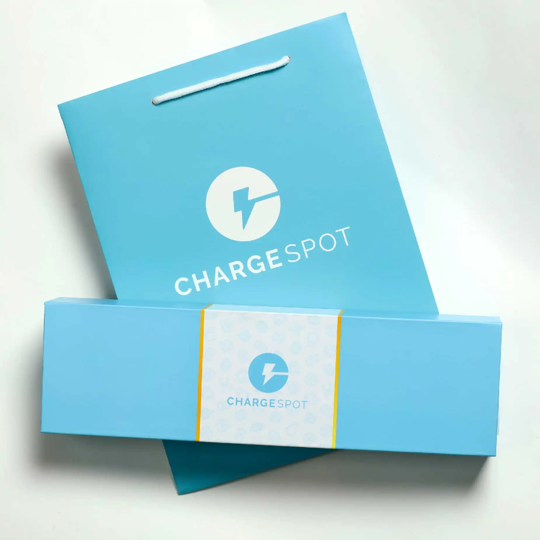 在白色的背景下，擺放了一個淺藍色的磁石書型硬盒，盒面印有"Chargespot"的字眼和商標，而盒的後方擺放了一個淺藍色的包裝袋。