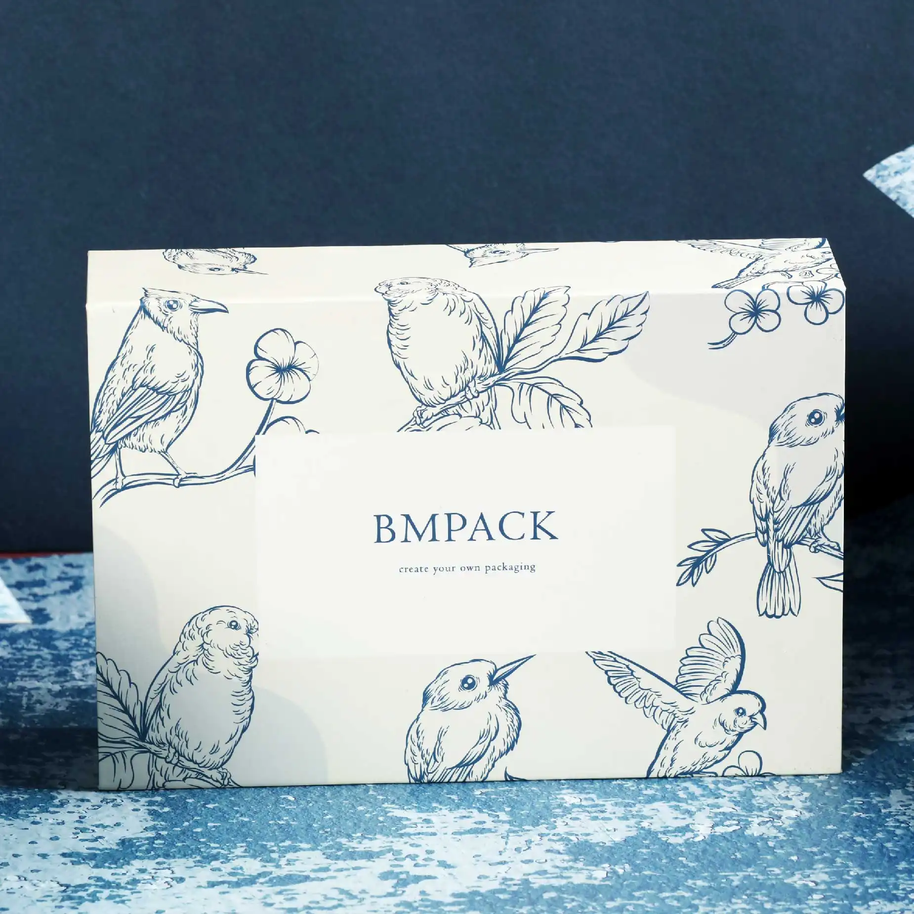 在深藍色的背景下，擺放了一個白色的磁石書型硬盒，盒面印有"BM Pack"的字眼加上深藍色的貓頭鷹圖案作點綴。